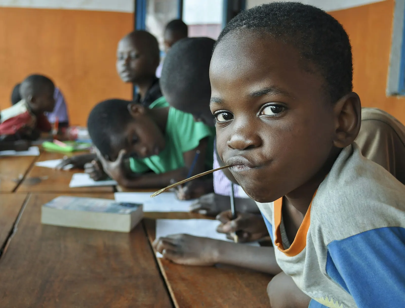 Children writing in class, a boy looking at the camera